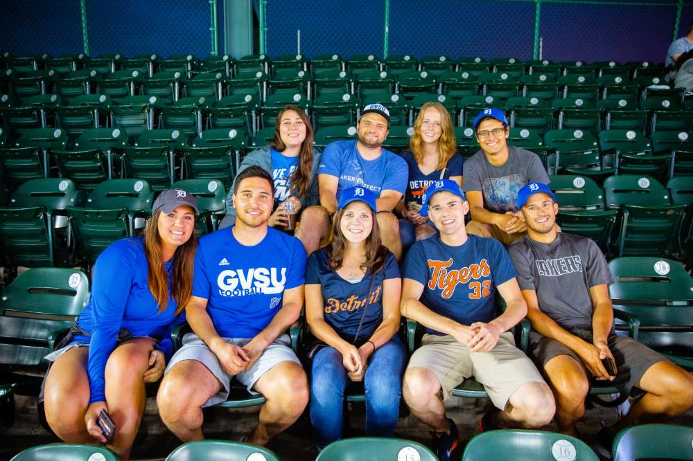 A group of nine gvsu tigers fans. 5 in the front row of seats and 4 in the back, all smiling